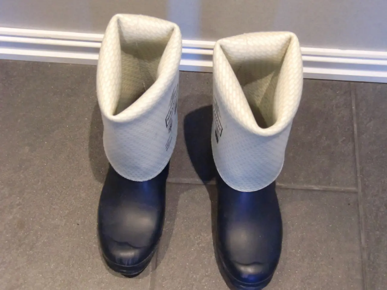 In the image there are two boots on the floor in front of a wall.