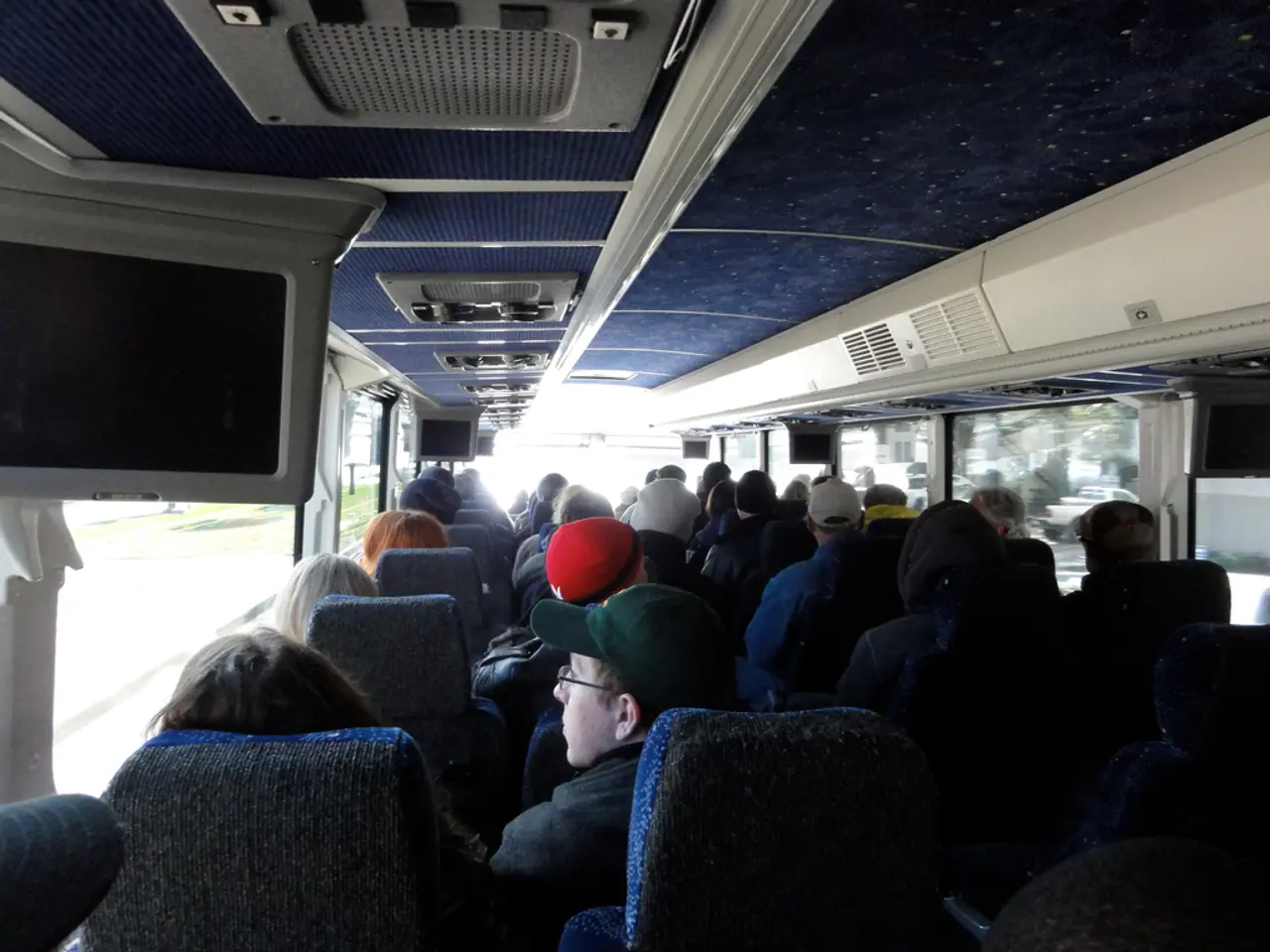 In the image there are many people sitting on the seats. And there are few with people with caps on...