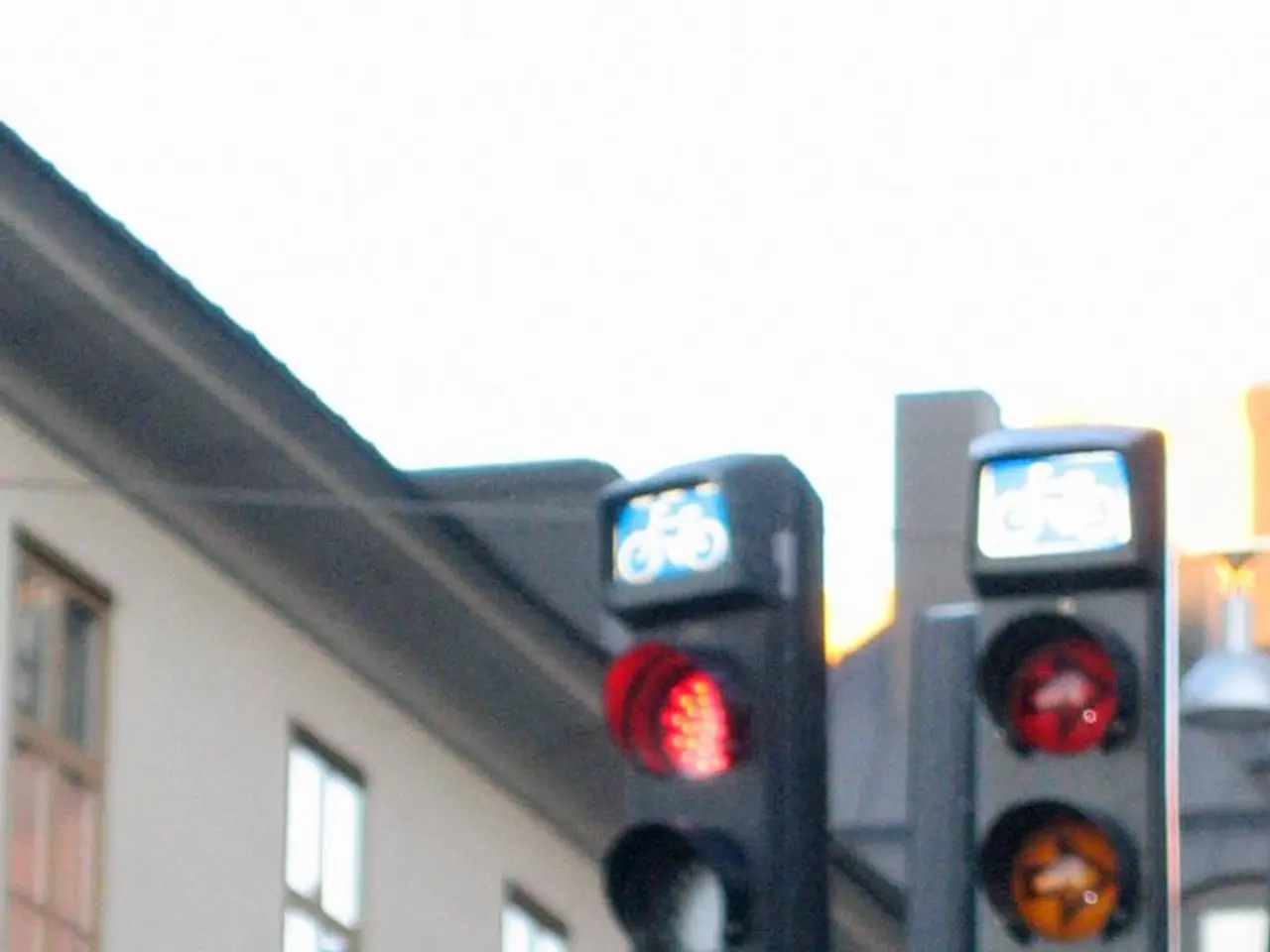 There is a building with windows on the left side. There are traffic signals with a pole on the...