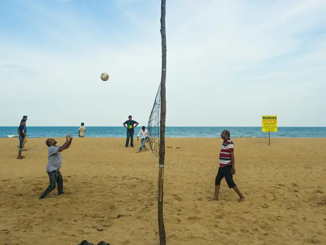 In the foreground of this image, there is a volleyball net to which on either side there are...
