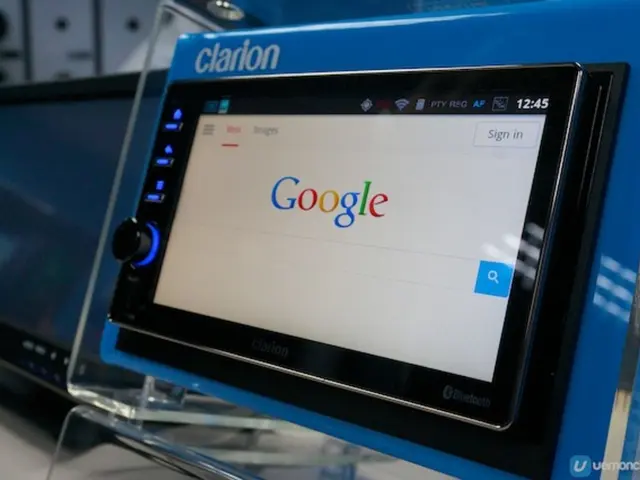 In the image there is a tablet on a stand, behind it there is a monitor on a table.