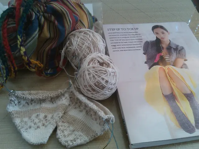 In this image there is a book, wool roll, cloth, papers on the table.